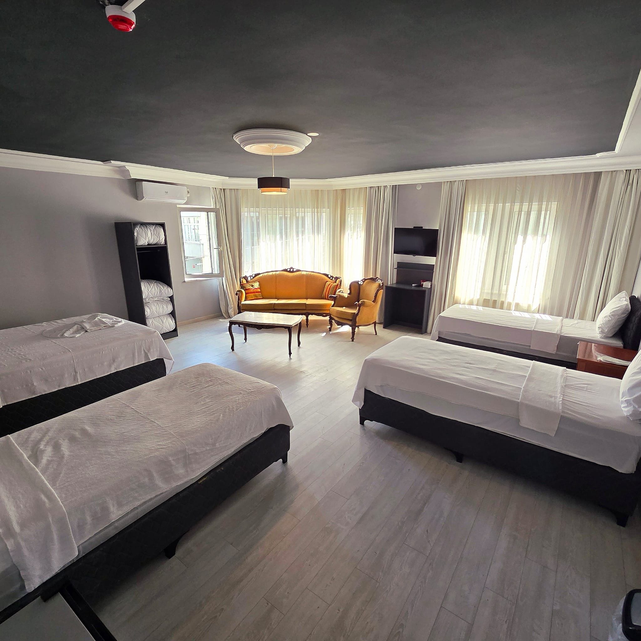 A hotel room with two single beds, a sofa, a TV, and a window with curtains.