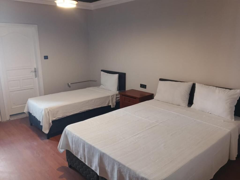 Quarto de hotel com duas camas de solteiro, uma mesinha de cabeceira de madeira e uma porta branca.