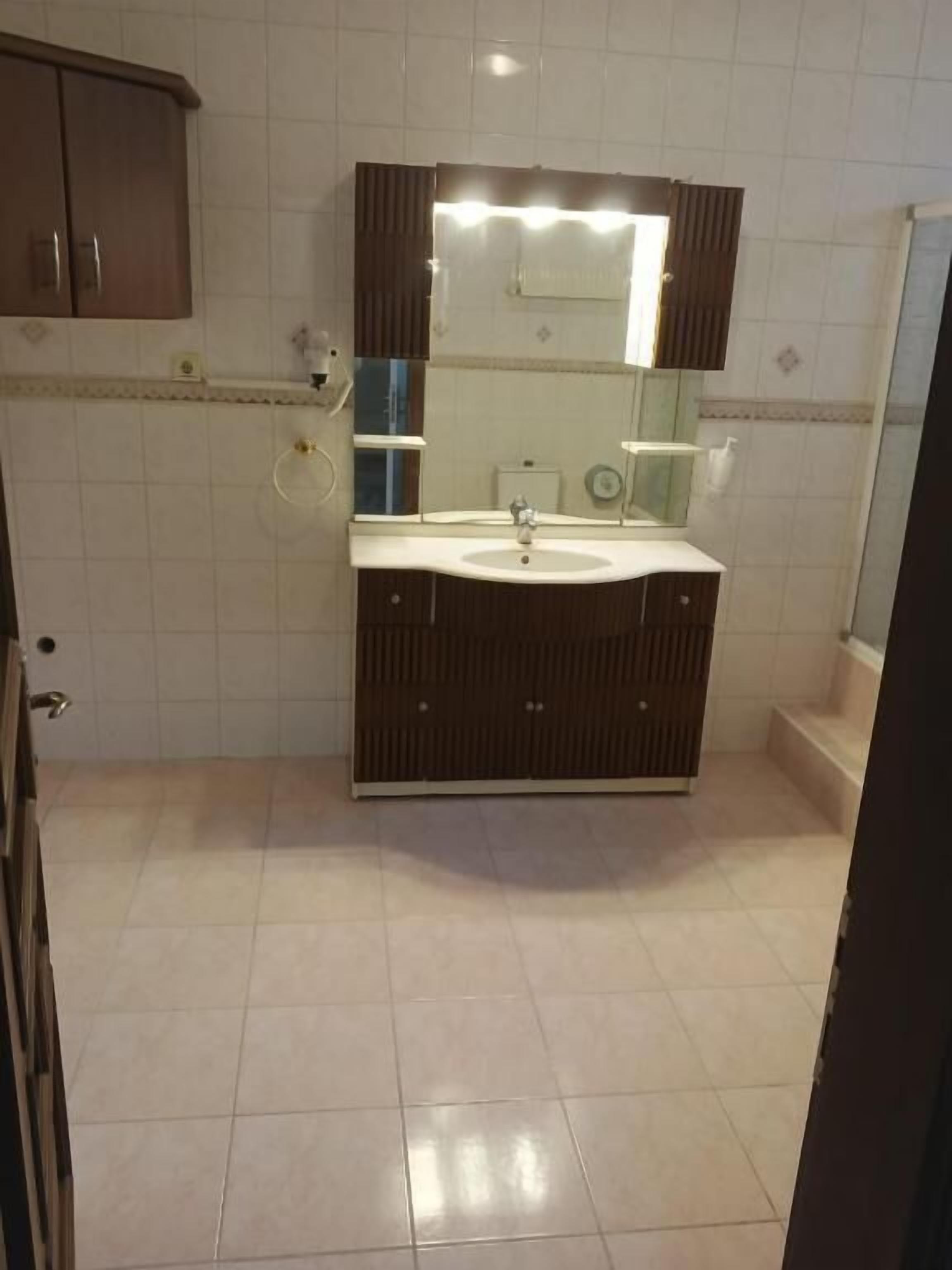 Un baño con lavamanos, espejo y piso de baldosas.