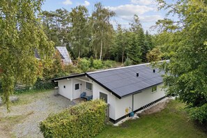 Une maison de plain-pied avec un toit en pente, un petit porche doté de deux chaises et une allée gravillonnée.