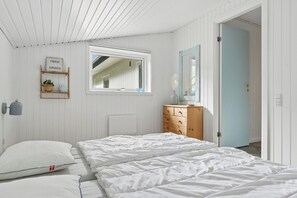 Une chambre à coucher comprenant un lit, une commode, un miroir, une fenêtre et une étagère fixée au mur, sur laquelle est posé un panneau.
