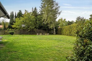 A well-maintained grassy backyard with a wooden fence, trees, and a clear sky. - Holiday home by the sea with hot tub (Væggerløse)