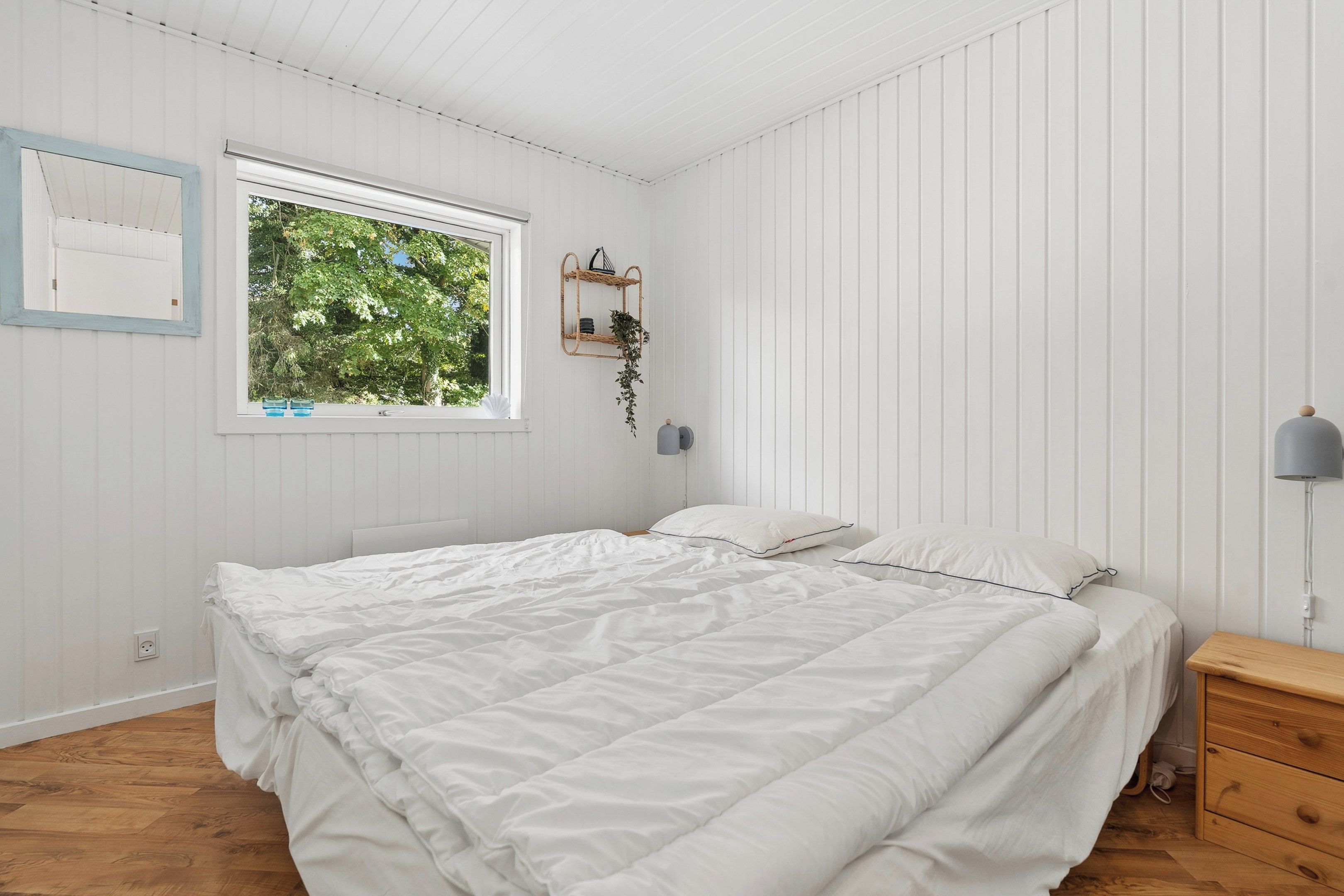 Een slaapkamer met een bed, een nachtkastje, een lamp, een raam en een wandplank.