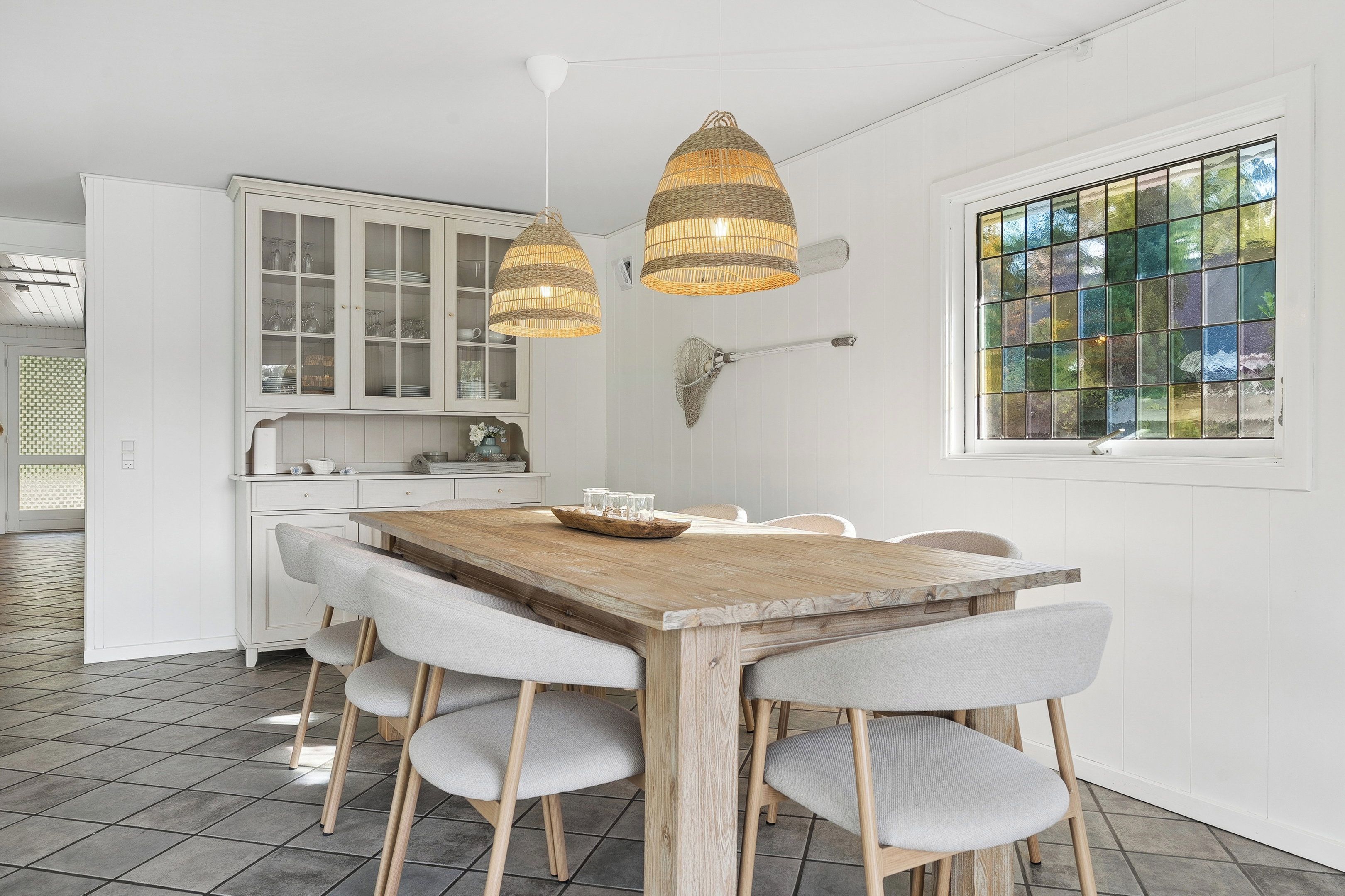 Un comedor con una mesa de madera, sillas tapizadas en gris y dos lámparas colgantes de mimbre.