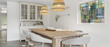 Un comedor con una mesa de madera, sillas tapizadas en gris y dos lámparas colgantes de mimbre.