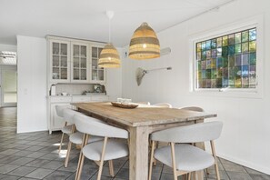 A dining area with a wooden table, grey upholstered chairs, and two hanging wicker lamps. - Holiday home by the sea with hot tub (Væggerløse)