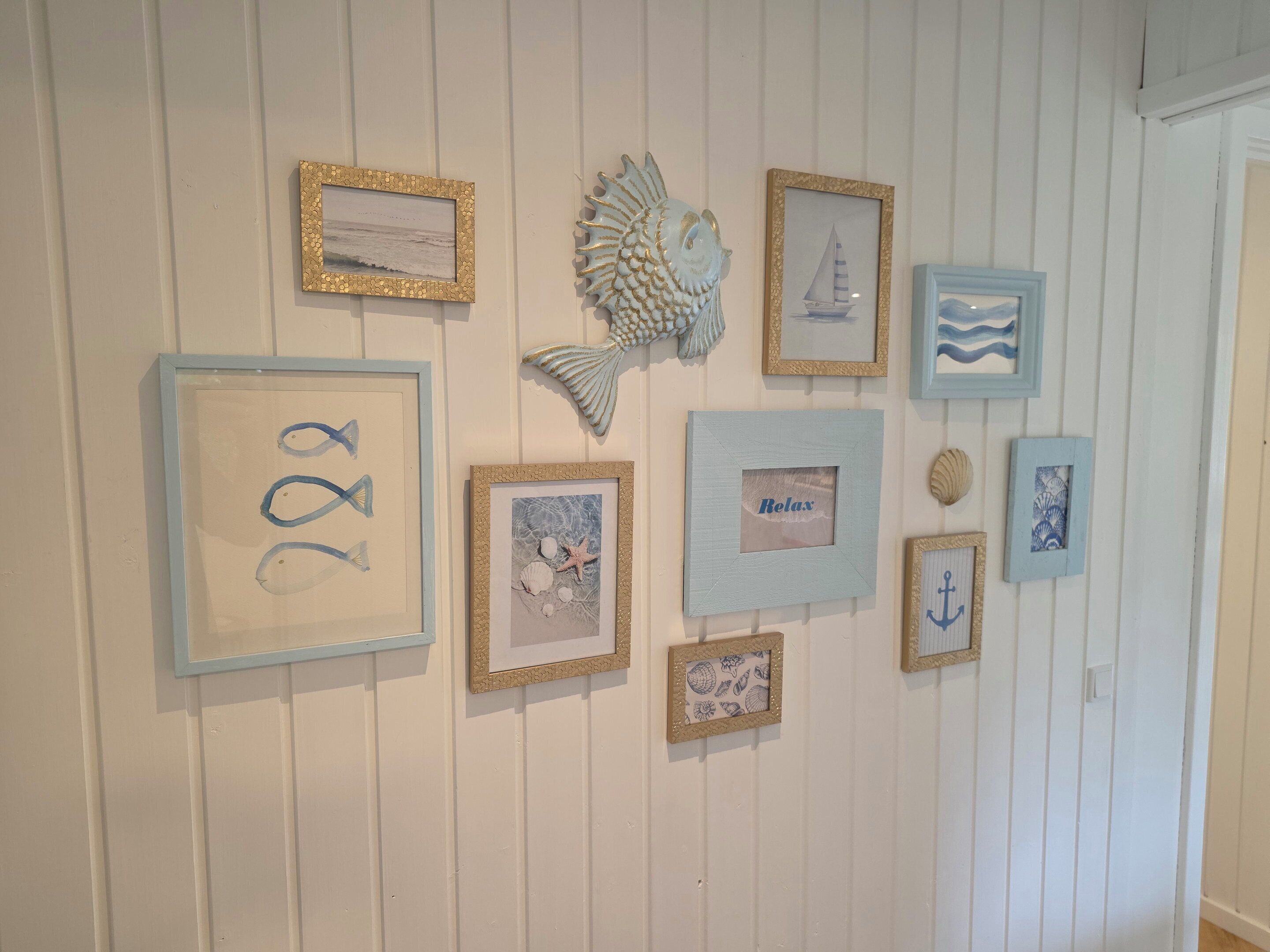A wall with various framed artworks and decorative items, including a fish sculpture and a sailboat.