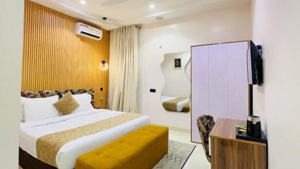 A modern hotel room with a large bed, a wooden headboard, a small desk, and a wall-mounted TV. - Defivez hotel  (Lekki)