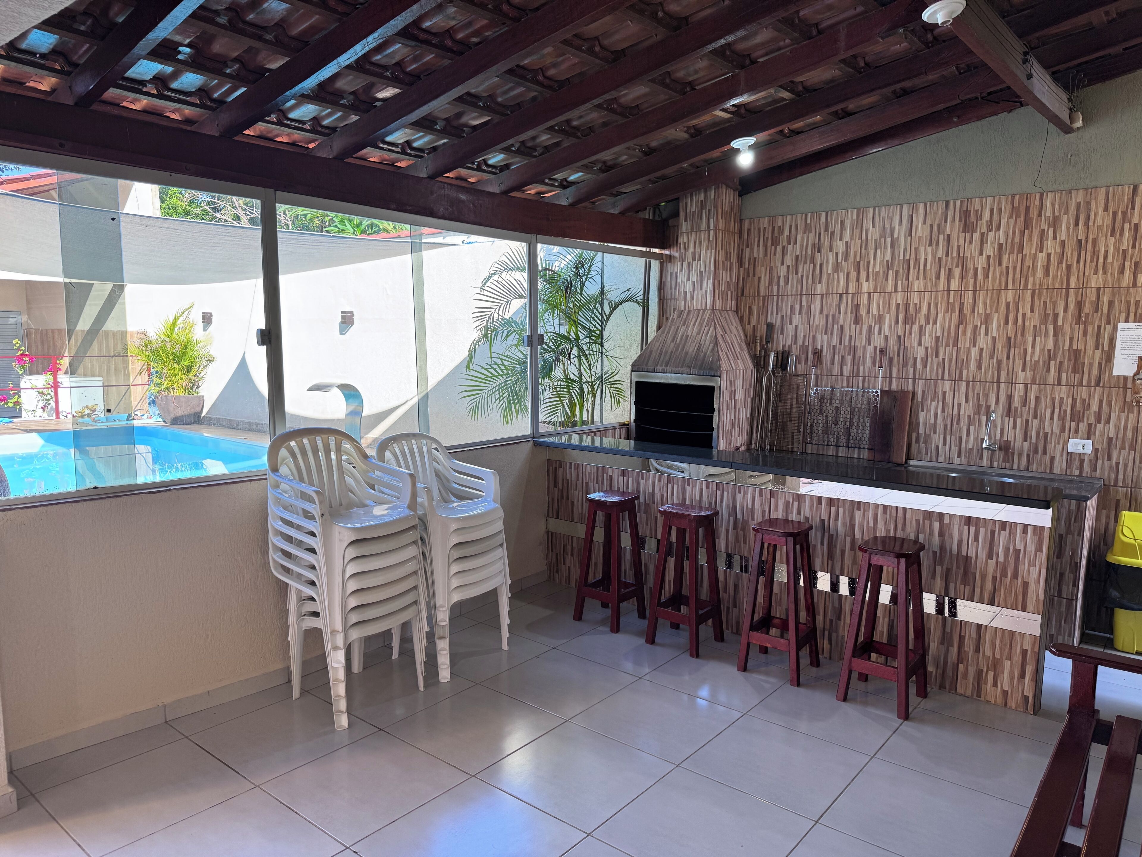 A kitchen with a built-in grill, bar stools, and a view of a swimming pool.