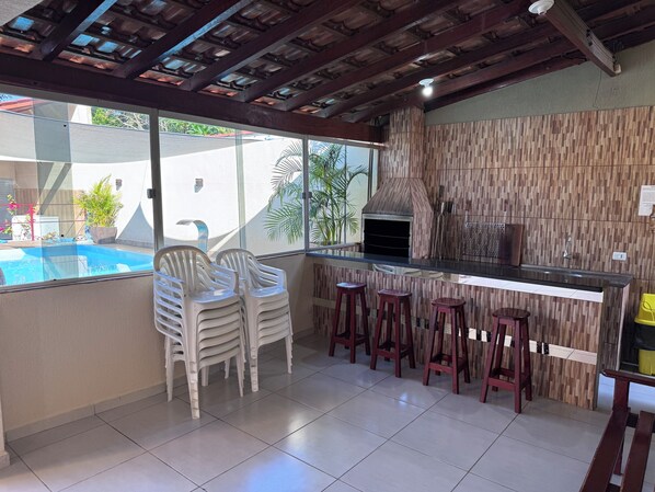 Une cuisine équipée d’un barbecue intégré, de tabourets de bar et offrant une vue sur une piscine.
