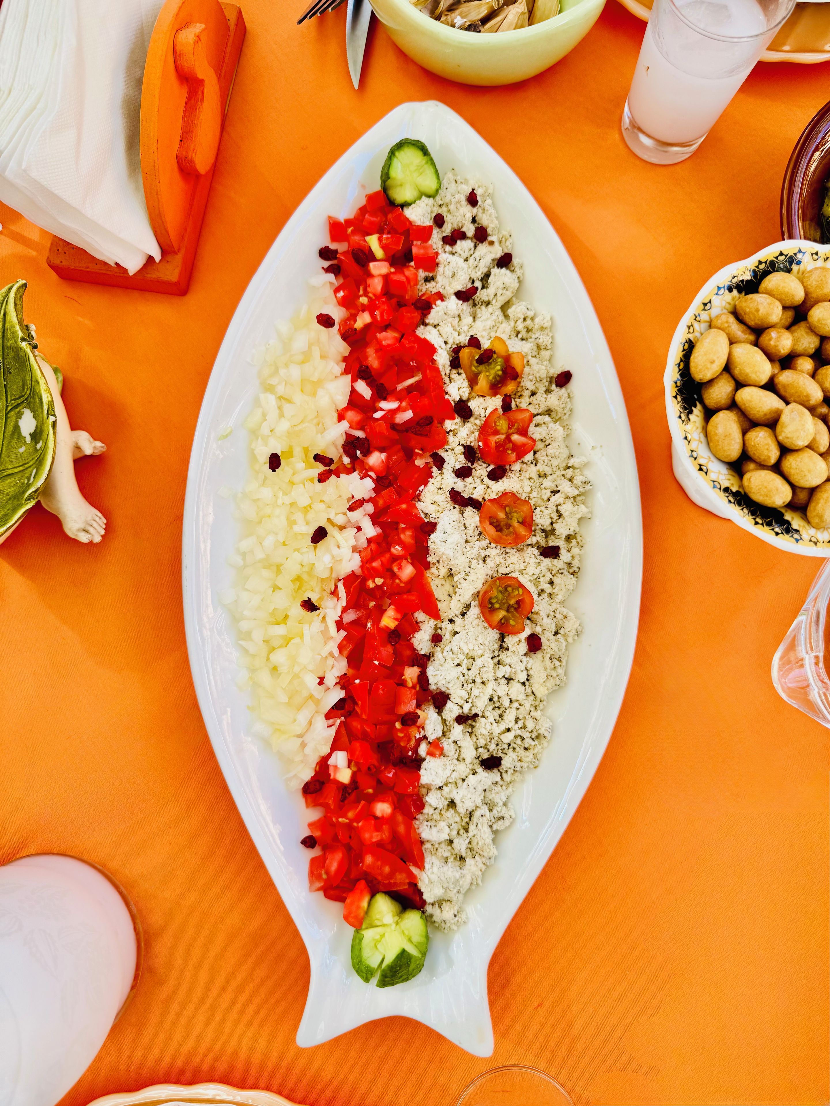 A white plate with rice, diced tomatoes, and cucumbers arranged on an orange tablecloth.