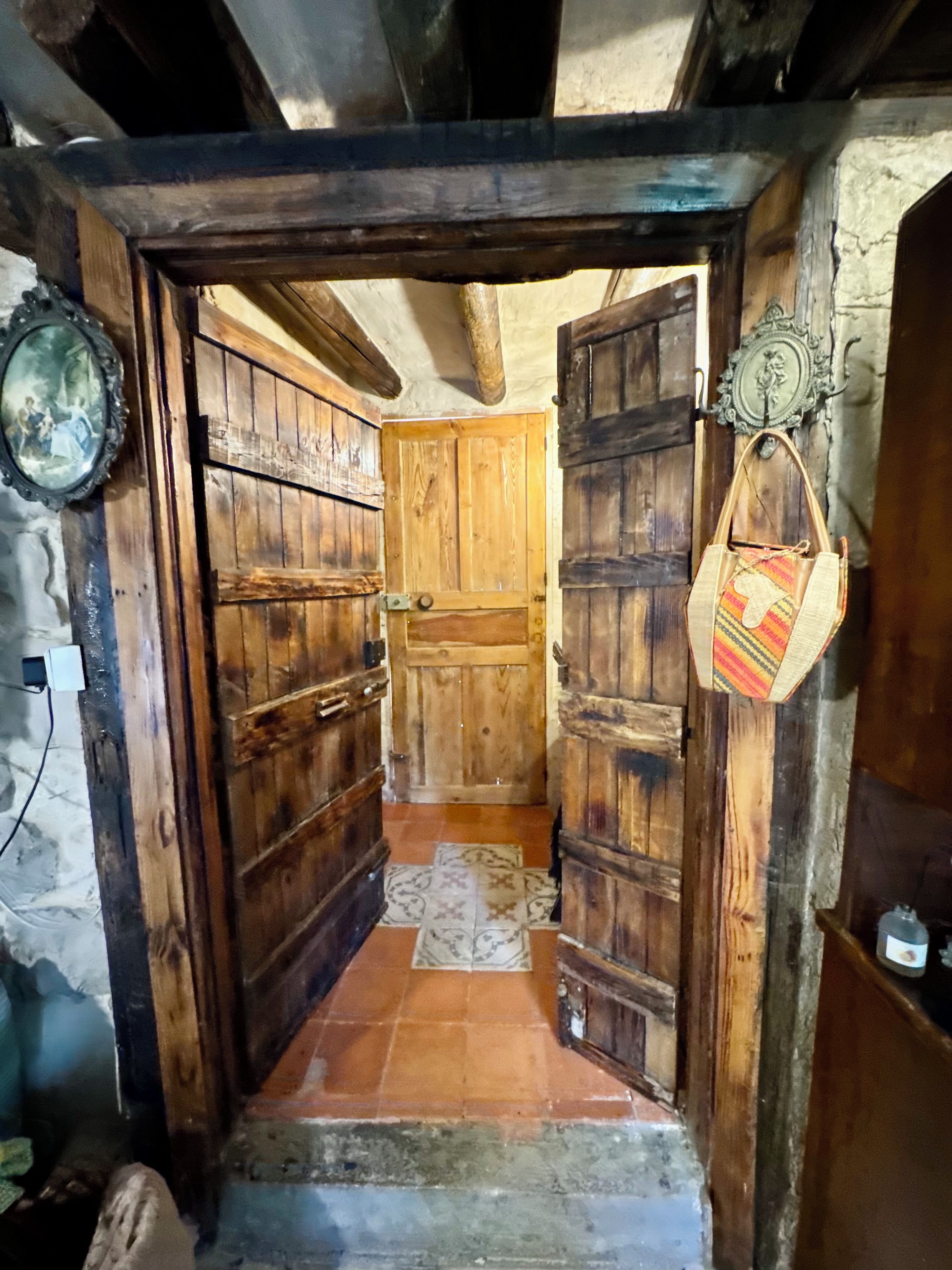 A narrow wooden hallway with a tiled floor leading to a room with a wooden door.