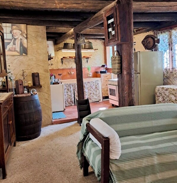 A rustic room with a bed, wooden furniture, a kitchen area, and a dining table.
