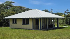 Een gelijkvloers huis met een veranda, omringd door een grasveld en bomen.