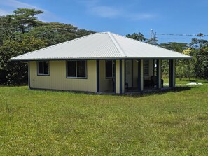Ein eingeschossiges Haus mit Veranda, umgeben von einer Wiese und Bäumen.