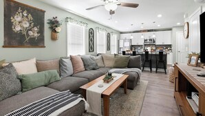 A living room with a sofa, coffee table, and a kitchen area with a bar and cabinets. - Mountain View Retreat with Hot Tub,Pet-Friendly,Near Asheville & Biltmore (Arden)