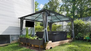 A covered garden area with raised beds, a wooden deck, and a house in the background. - Mountain View Retreat with Hot Tub,Pet-Friendly,Near Asheville & Biltmore (Arden)