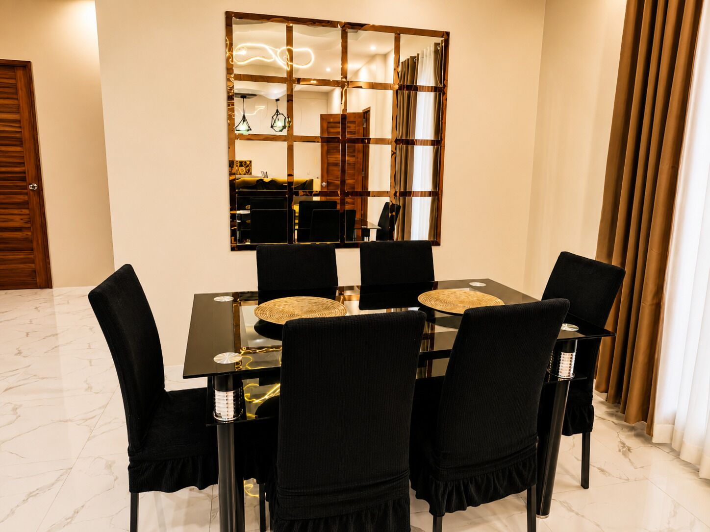 Un coin repas comprenant une table noire, quatre chaises noires, un miroir décoratif et un luminaire moderne.