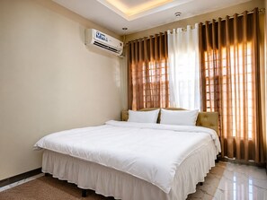 A hotel room with a large bed, an air conditioning unit, and curtains.