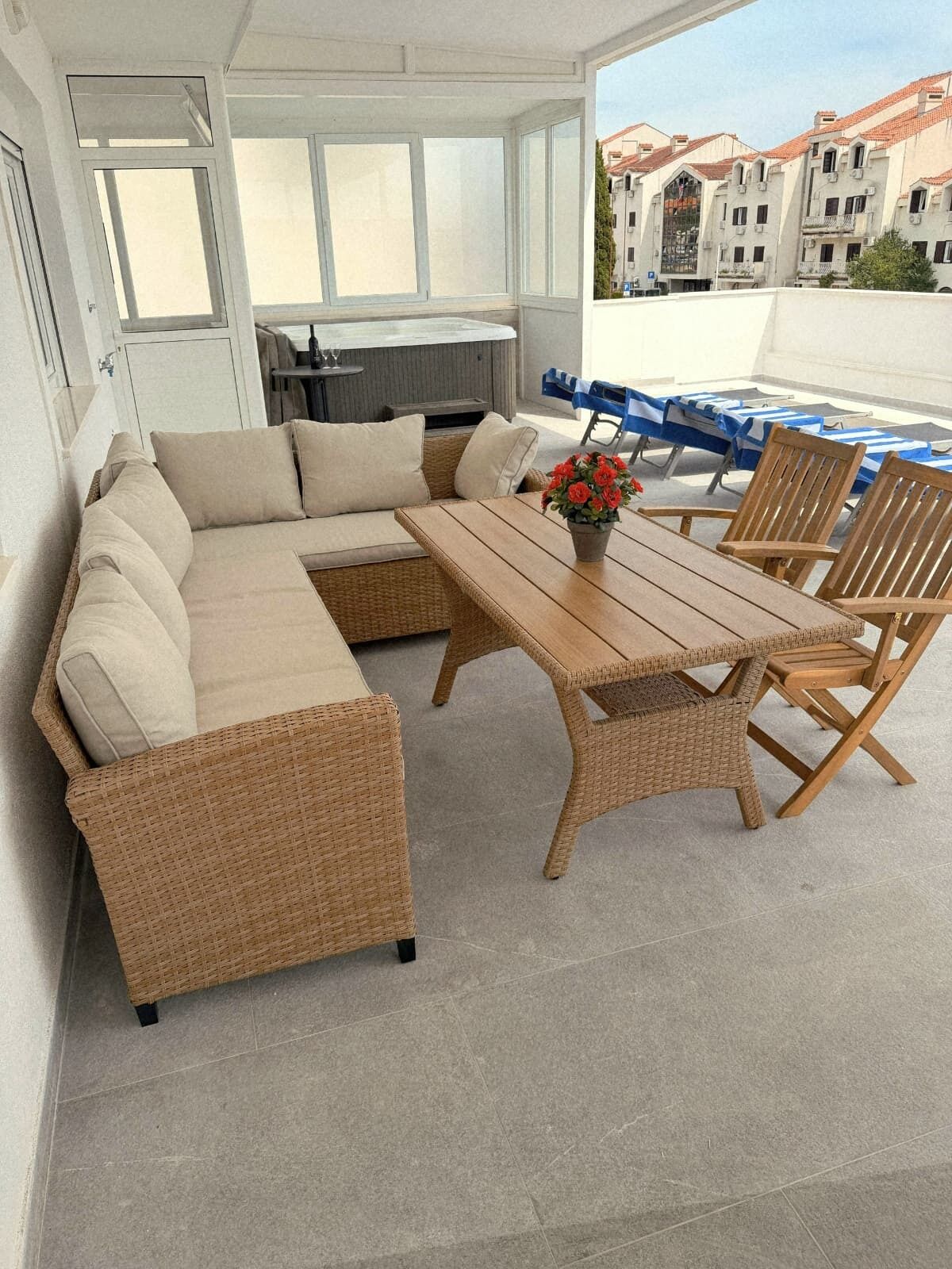 En solig uteservering med en soffa av rotting, ett träbord och stolar, med utsikt över stadsbilden.