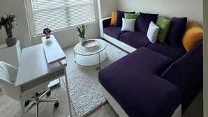 A modern living room with a white desk, purple sofa, and a small white table with a bowl. - Perfect for Nurses-Charming 2-bedroom townhome in Atlanta Metro (Lithonia)