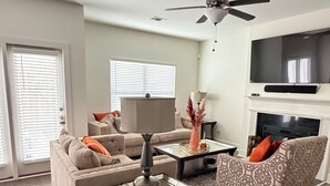 A living room with a sofa, two armchairs, a coffee table, a fireplace, a ceiling fan, and a TV mounted on the wall. - Perfect for Nurses-Charming 2-bedroom townhome in Atlanta Metro (Lithonia)