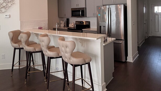 A modern kitchen with a central island, stainless steel appliances, and a bar area with stools. - Perfect for Nurses-Charming 2-bedroom townhome in Atlanta Metro (Lithonia)