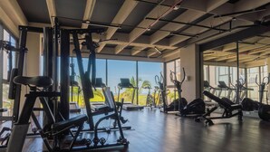 Ein Fitnessstudio mit unterschiedlichen Trainingsgeräten, großen Fenstern und Blick auf Palmen.