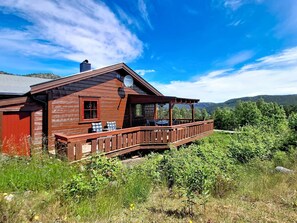 A wooden cabin with a porch, a satellite dish, and a view of the surrounding forest and hills. - Bjørnbu by Interhome (Eikerapen)