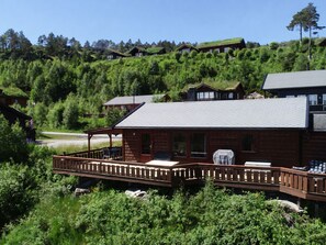 A wooden cabin with a deck, surrounded by dense greenery and other cabins on a hillside. - Bjørnbu by Interhome (Eikerapen)