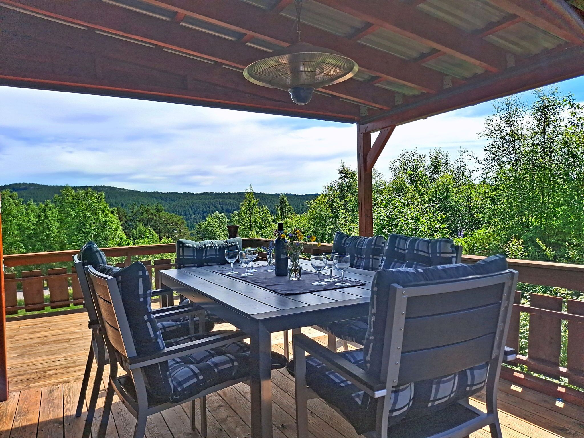 A covered outdoor dining area with a table and chairs, a fan, and a scenic view of hills and trees.