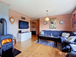 A cozy living room with a wood-burning stove, a sofa, a TV, and a dining area. - Bjørnbu by Interhome (Eikerapen)