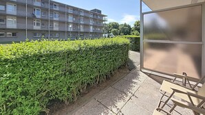 Ein Wohngebäude mit mehreren Balkonen, einer gepflegten Hecke und einem überdachten Außenbereich mit Sitzgelegenheiten.