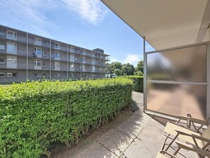 A residential building with multiple balconies, a well-maintained hedge, and a covered outdoor area with chairs. - Hyacint with parking by Interhome (De Haan)