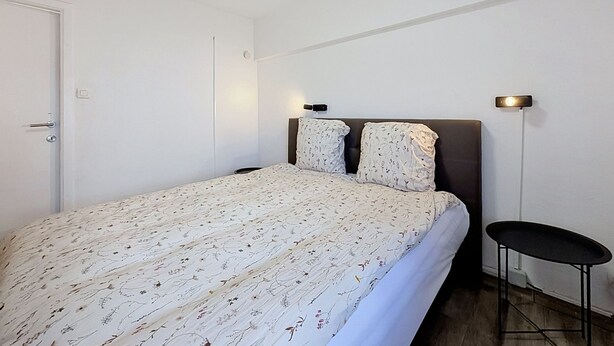 Ein Schlafzimmer mit Bett, Nachttisch, Wandlampe und Tür.