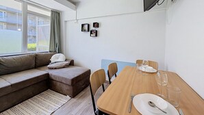 Ein modernes Wohnzimmer mit einer Couch, einem Esstisch für zwei Personen und einem an der Wand befestigten Fernseher.