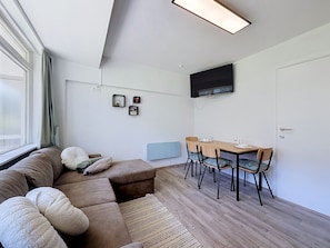 A modern living room with a sofa, a dining table with chairs, a flat-screen TV mounted on the wall, and a window with curtains. - Hyacint with parking by Interhome (De Haan)
