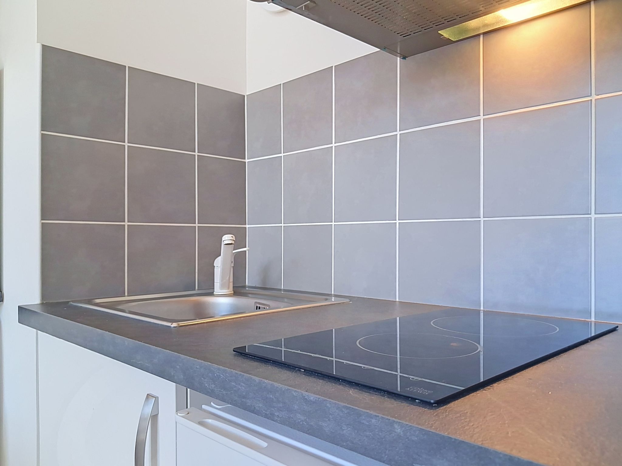 A kitchen with a built-in induction cooktop, a stainless steel sink, and grey tiles.