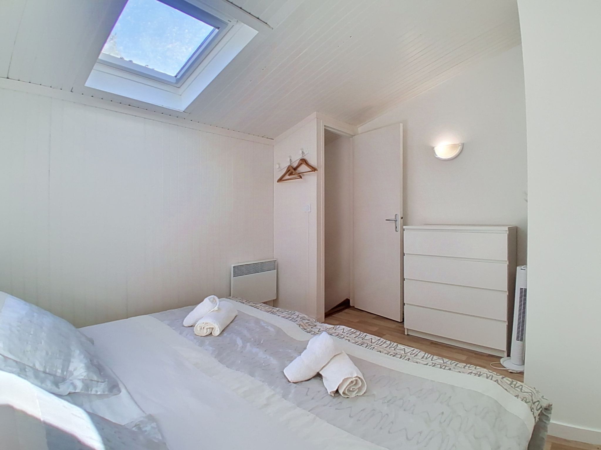 A bedroom with a skylight, a bed with rolled towels, a radiator, and a wardrobe.