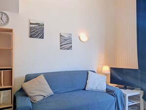 Ein Zimmer mit einem blauen Sofa, zwei Kissen, einer Wanduhr und zwei gerahmten Bildern.