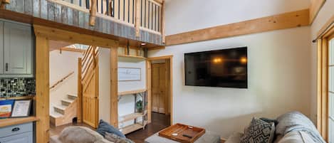 Uma sala de estar espaçosa com pé direito alto, escada de madeira, TV de tela plana na parede e um agradável espaço de estar.