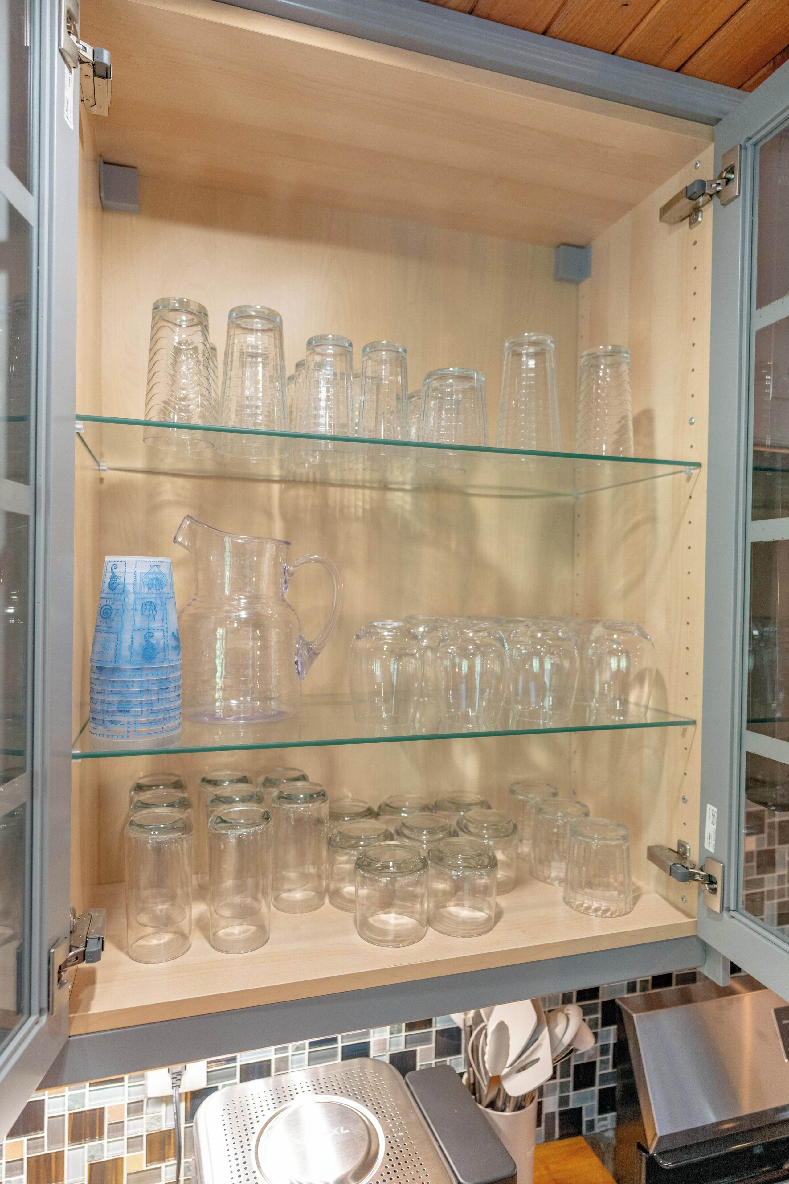 A kitchen cabinet with multiple shelves holding various glassware items.