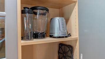 A kitchen cabinet with a blender, a kettle, and a fan on the shelf.