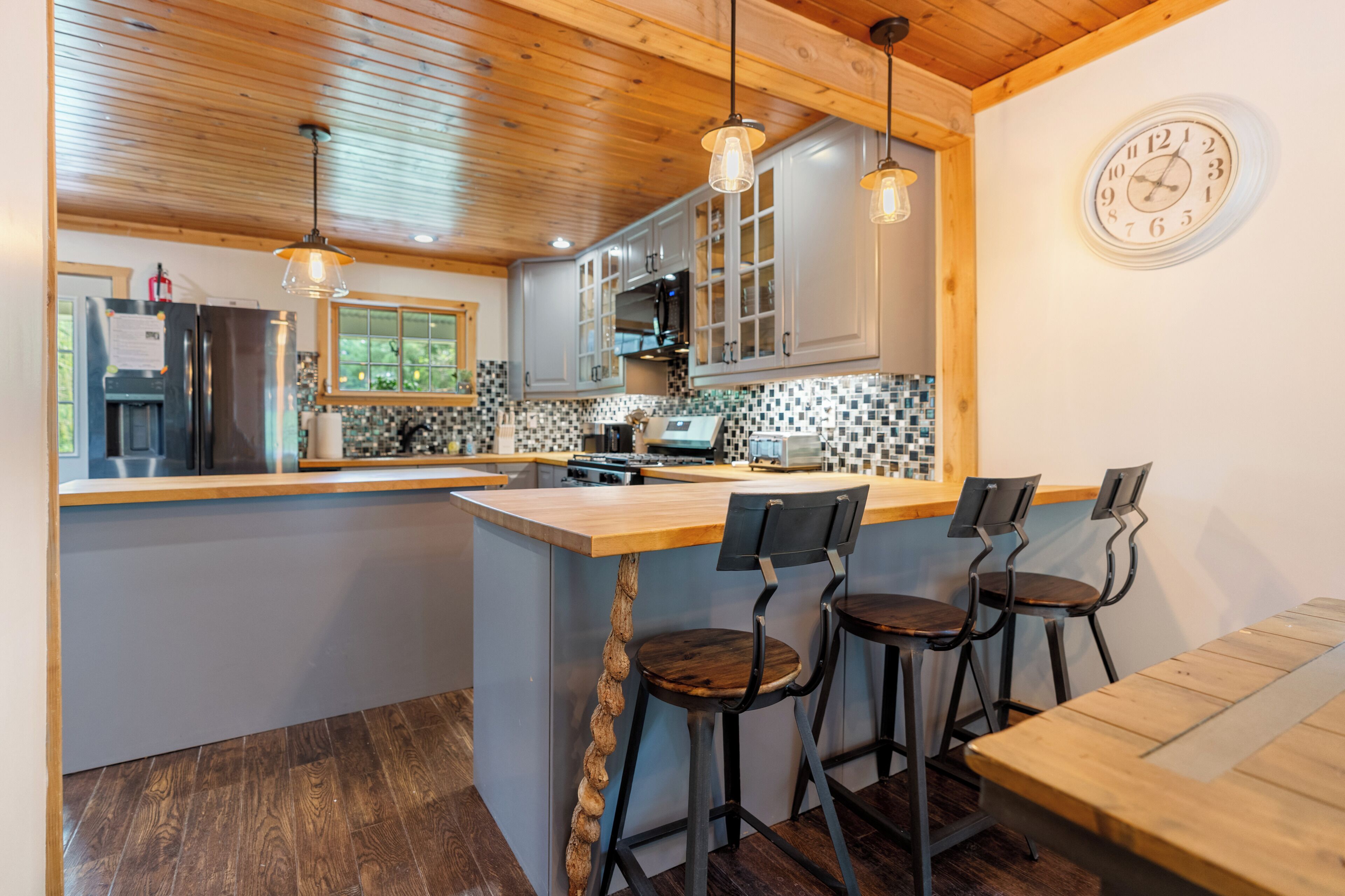 Una cocina moderna con una isla central, taburetes de bar y un reloj en la pared.