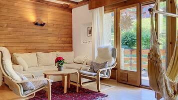 A cozy room with a wooden ceiling, a white sofa, a white chair, a red patterned rug, and a hammock.