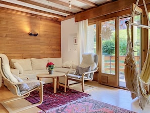A cozy room with a wooden ceiling, a white sofa, a white chair, a red patterned rug, and a hammock. - Chalet Chaudoudoux - Les Paccots by Interhome (Les Paccots)