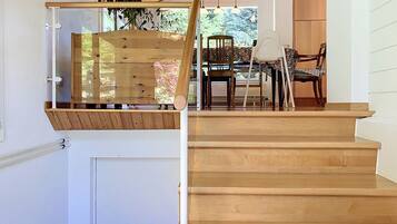 A wooden staircase with a glass railing, a dining area with chairs and a table, and a view of greenery outside.
