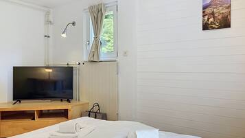 A hotel room with a bed, a TV, a window with curtains, a radiator, and a painting on the wall.