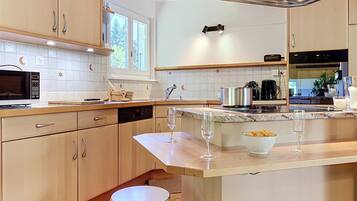 A kitchen with wooden cabinets, a microwave, a sink, and a countertop with two wine glasses and a bowl of chips.