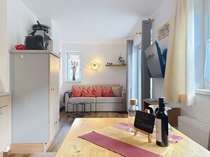 A cozy living room with a sofa, a coffee table, and a dining area with a table and wine bottle. - Ferienhaus Gundi by Interhome (Pettneu am Arlberg)